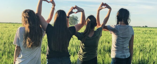 Image shows young people sitting outside creating heart shapes with their hands