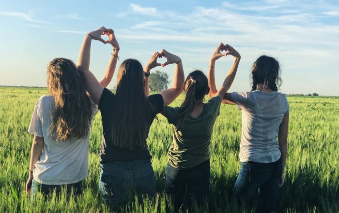 Image shows young people sitting outside creating heart shapes with their hands