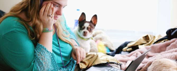 person on bed with dog, wearing headphones looking at laptop