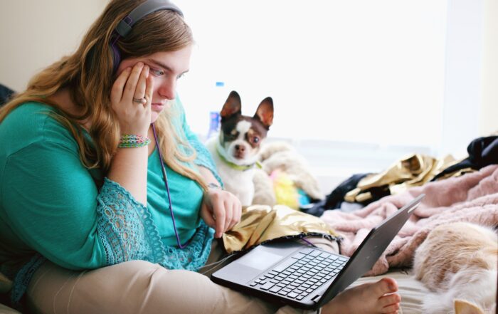 person on bed with dog, wearing headphones looking at laptop